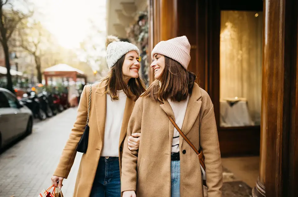 To jenter i beige kåpe smiler mot hverandre på gata