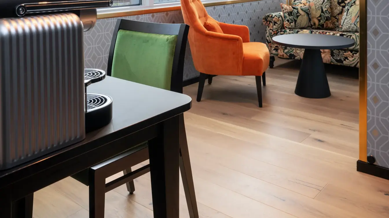 Skrivebord med kaffemaskin og grønn stol. Sittegruppe med fargerik sofa, oransje stol og sort rundt bord og store vinduer med utsikt i junior suite på Thon Hotel Cecil