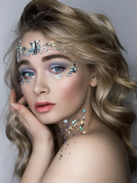 Dame sminket med sølvstener i panne og rundt øynene og glitter på halsen