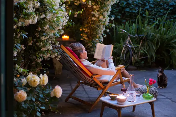 dame som sitter i lenestol, ute i hagen med en bok