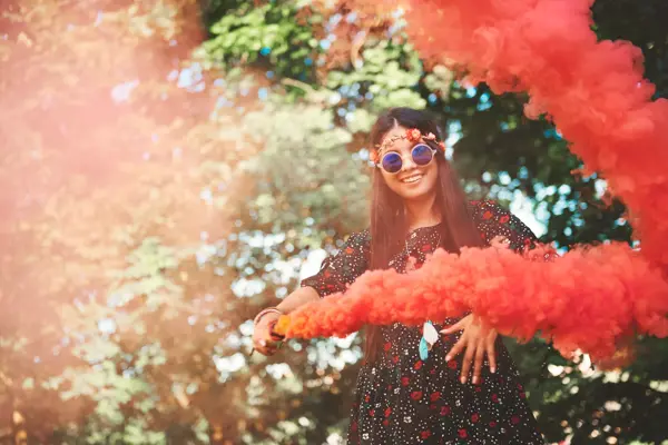 Jente med blomsterkrans og runde solbriller holder en rød/oransje fargebombe