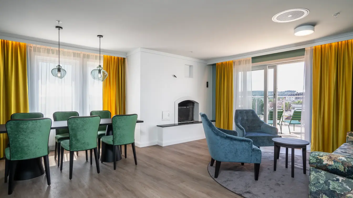 Peis, sofa, veranda, gule gardiner, 2 blå lene stoler, salongbord, parkettgulv, spisebord, 6 grønne stoler, vindu