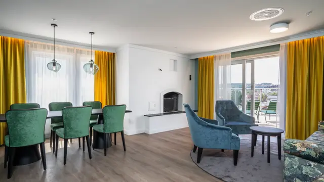 Peis, sofa, veranda, gule gardiner, 2 blå lene stoler, salongbord, parkettgulv, spisebord, 6 grønne stoler, vindu
