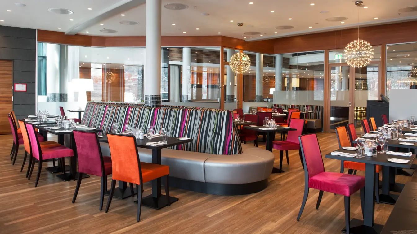 Restaurant med rosa og oransje stoler og detaljer, bord, stoler og sofa.