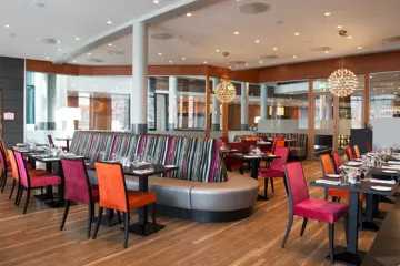 Restaurant med rosa og oransje stoler og detaljer, bord, stoler og sofa.