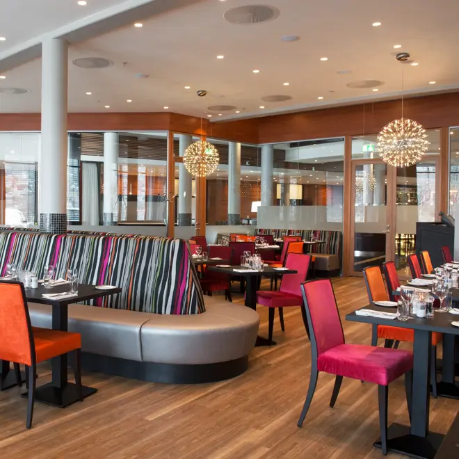 Restaurant med rosa og oransje stoler og detaljer, bord, stoler og sofa.