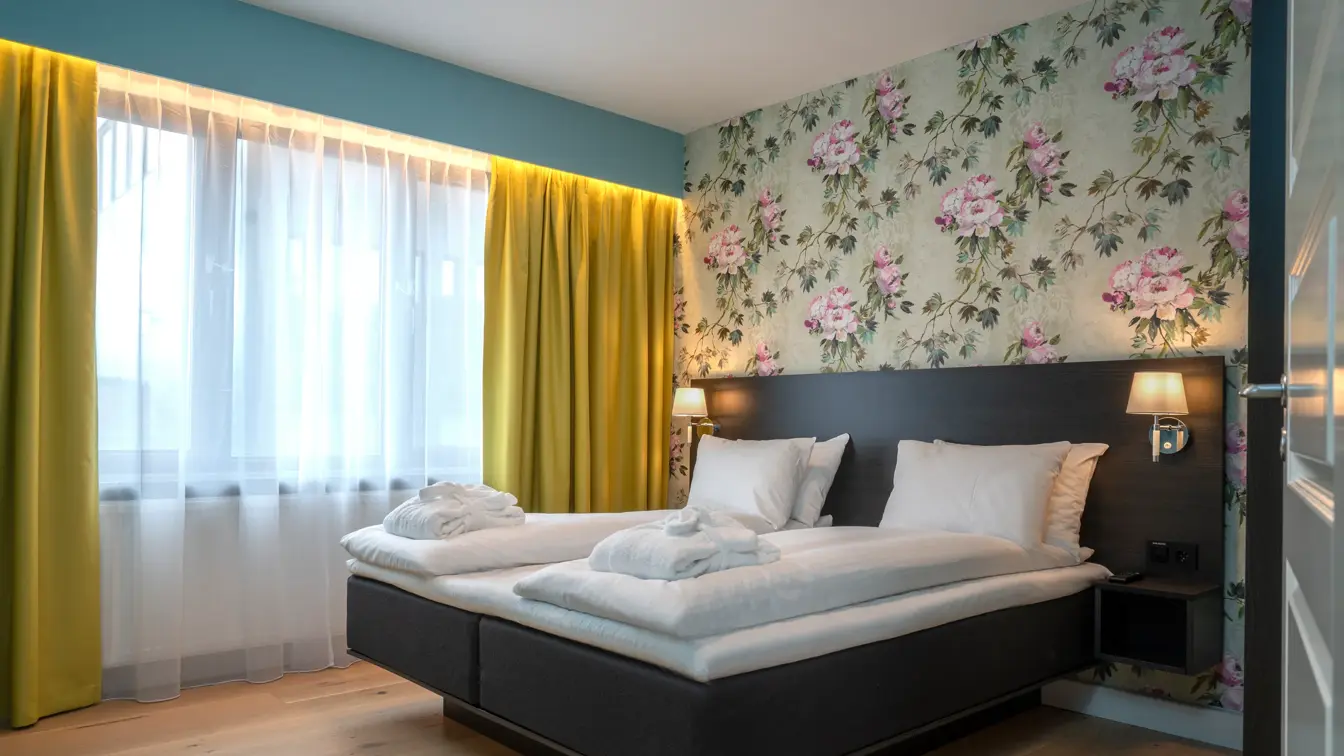 Tapetvegg, dobbeltseng, vindu fra gulv til tak, parkettgulv, gule gardiner. 