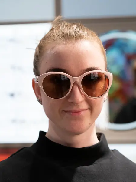 Jente med håret satt opp i stram topp, og sort genser har på seg lyserosa solbriller fra Gucci