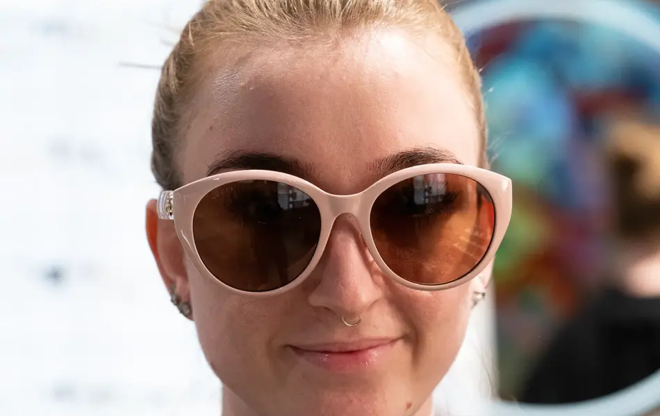 Jente med håret satt opp i stram topp, og sort genser har på seg lyserosa solbriller fra Gucci