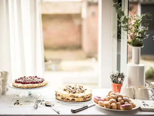 Utsnitt av kakebord med hvit duk og tre ulike kaker. Foto til artikkel om ting å huske på når du skal arrangere konfirmasjon.