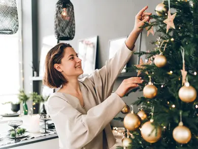 Nærbilde av dame som smiler mens hun pynter juletre med julekuler av gull