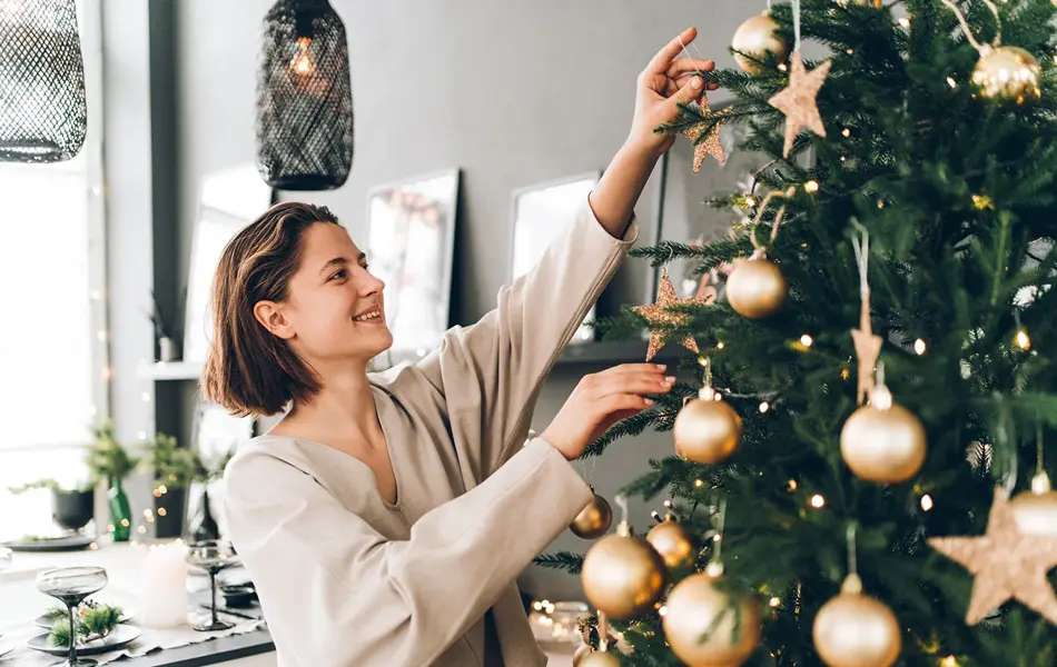 Nærbilde av dame som smiler mens hun pynter juletre med julekuler av gull