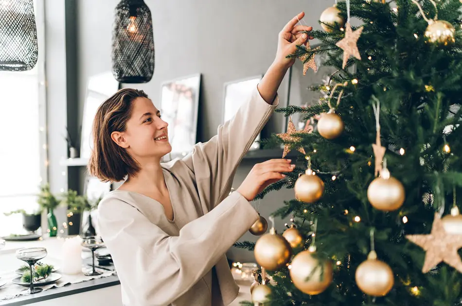 Nærbilde av dame som smiler mens hun pynter juletre med julekuler av gull