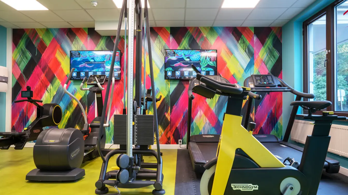 Tapetvegg i forskjellige farger, vindu, gult gulv, diverse apparater. 