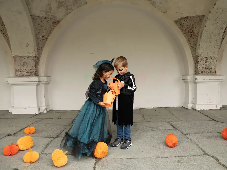 To barn som ser i en godteribøtte til halloween