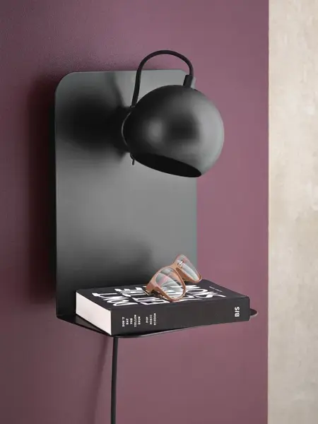 Vegglampe med liten hylle med en bok på.