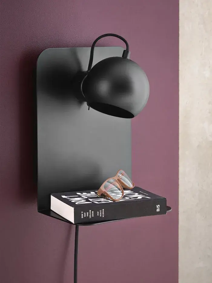 Vegglampe med liten hylle med en bok på.