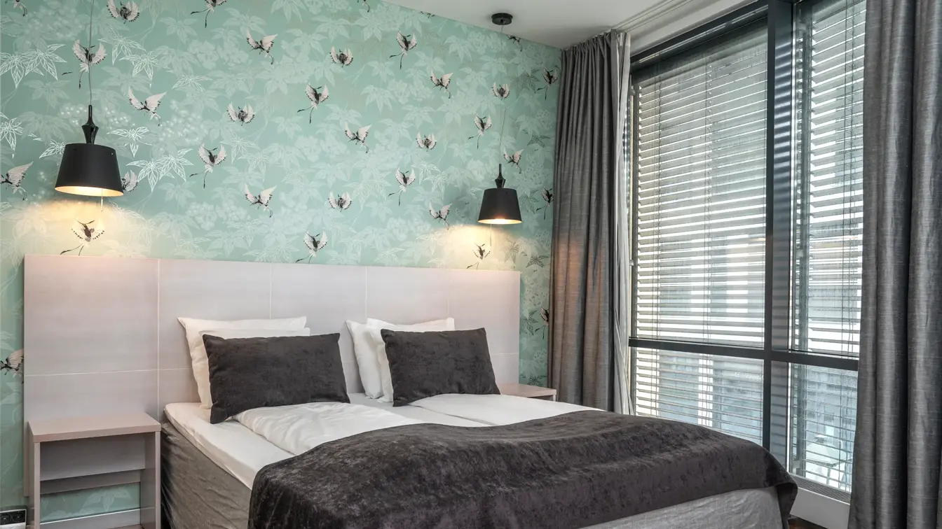 Suite med sjøgrønn, mønstrete tapet, dobbeltseng og gulv-til-tak-vinduer.