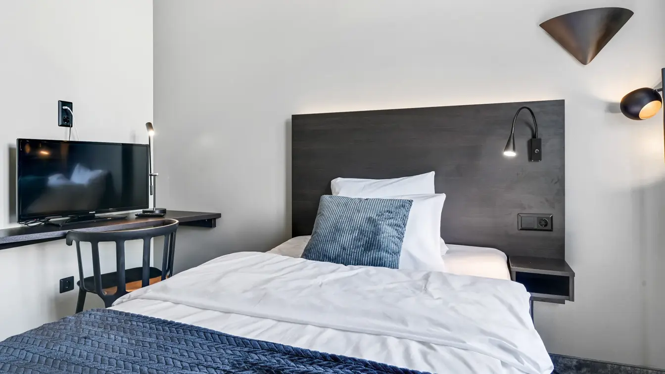 Enkeltseng, hvite vegger, TV, skrivebord, stol. 