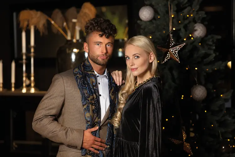 Par i pentøy foran glamorøst juletre