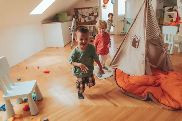Photo of a cheerful boys, running in a circles around wigwam tent in their playroom