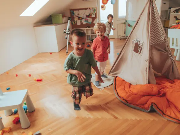 Photo of a cheerful boys, running in a circles around wigwam tent in their playroom