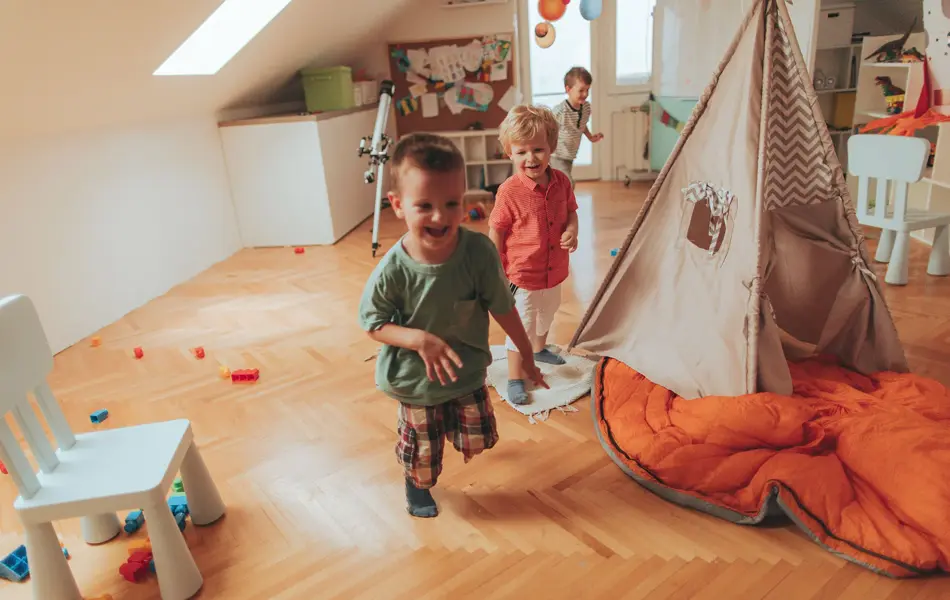 Photo of a cheerful boys, running in a circles around wigwam tent in their playroom