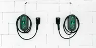 To ladekabler til el-bil henger på hvit vegg.