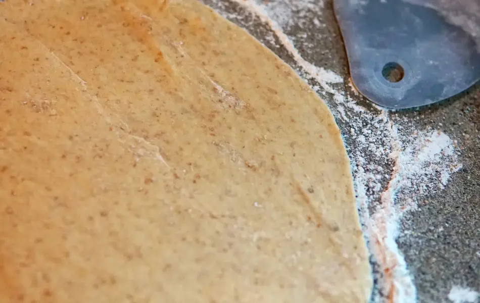 deigen er kjevlet ut på en benk, omringet av mel