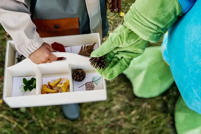 oskar som legger kongle i en kasse holdt av et barn
