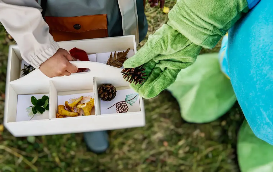 oskar som legger kongle i en kasse holdt av et barn