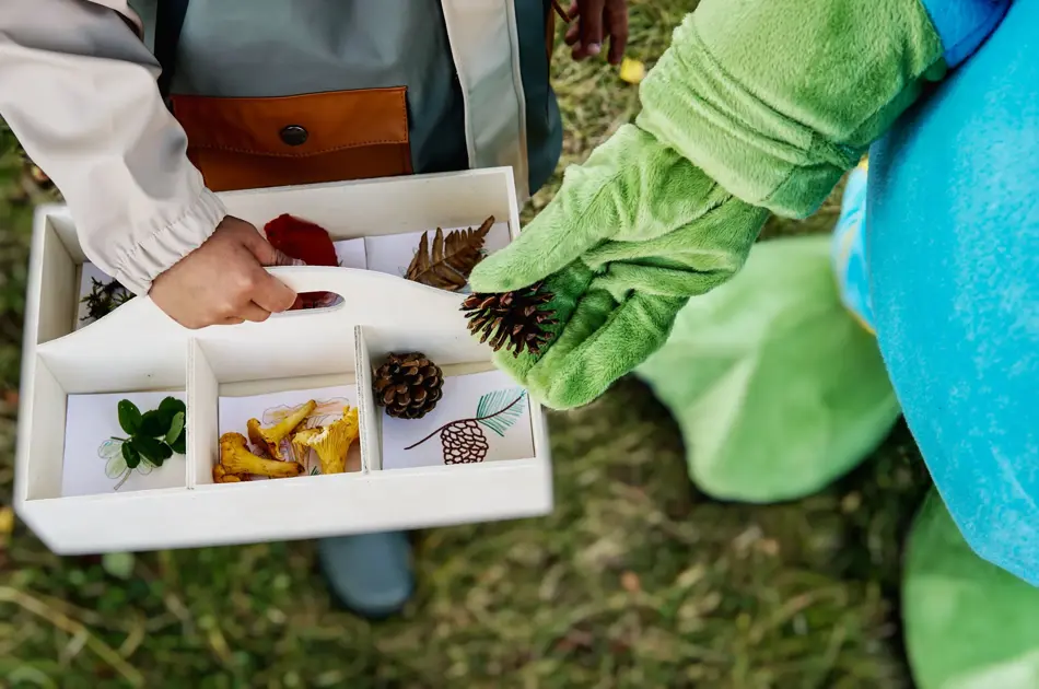 oskar som legger kongle i en kasse holdt av et barn