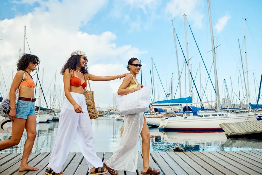 Tre sommerkledde damer vandrer på båtbrygge. 