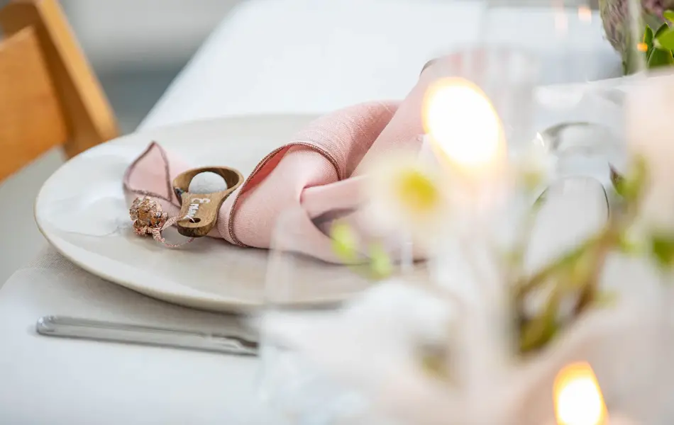 Langbord dekker til gjester med rosa servietter og grønn naturlig dekorasjon