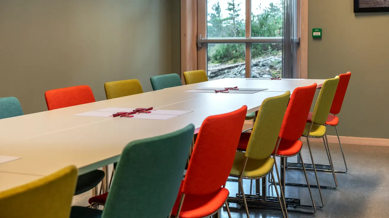 Møterom med styrebordsoppsett zoomet inn på bordet med fargerike stoler rundt. 