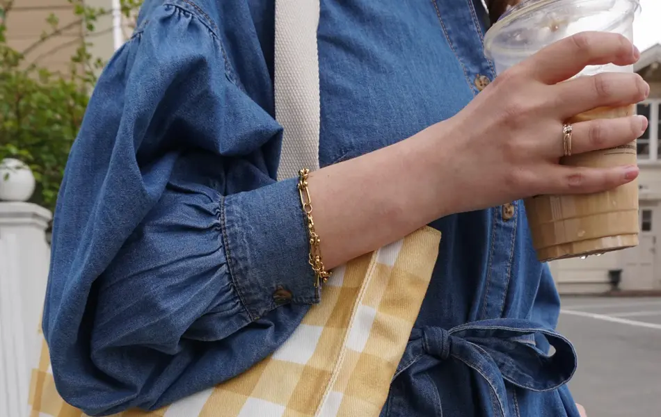 Nærbilde av kvinne med olakjole, rutete veske og en kaffekopp i hånden