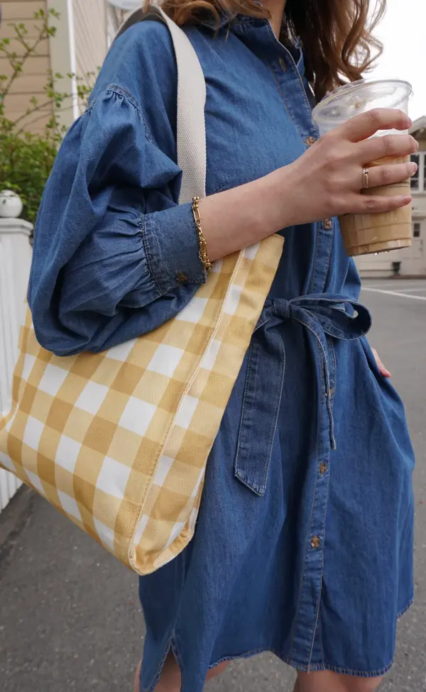 Nærbilde av kvinne med olakjole, rutete veske og en kaffekopp i hånden