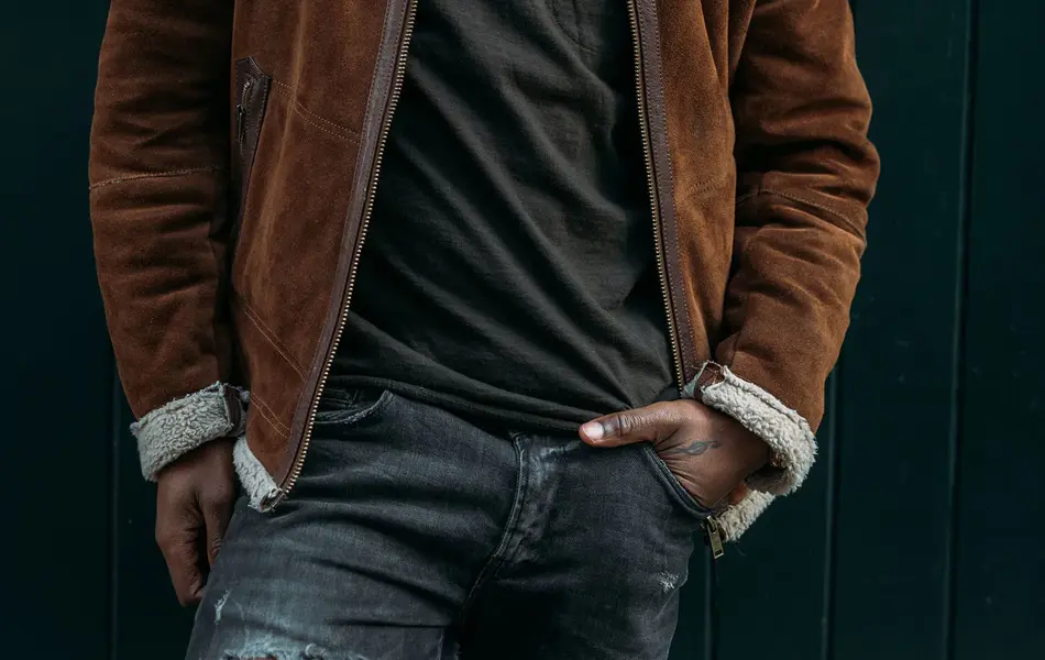 Mann i brun, semsket skinnjakke og grønn lue poserer foran vegg 