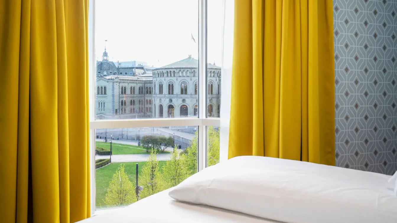 Gule gardiner og store vinduer med utsikt over Stortinget i junior suite på Thon Hotel Cecil