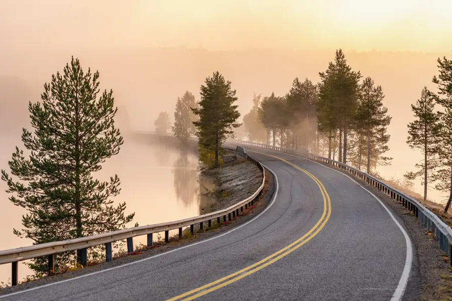 Finnish landscape with narrow car road through the lake. Foggy early morning in autumn in Finland