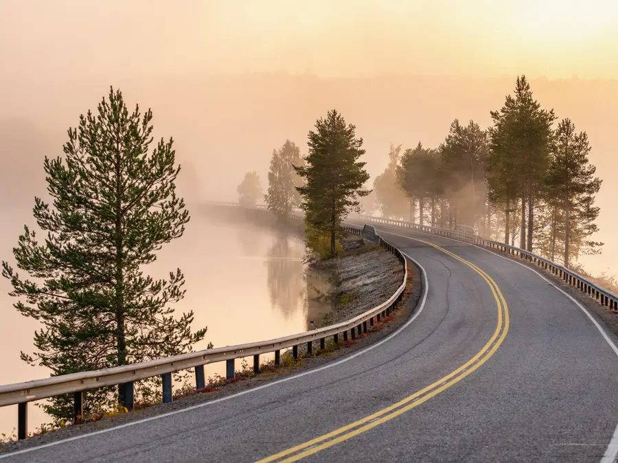 Finnish landscape with narrow car road through the lake. Foggy early morning in autumn in Finland
