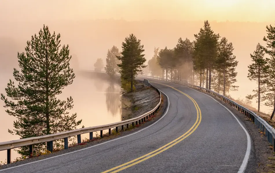 Finnish landscape with narrow car road through the lake. Foggy early morning in autumn in Finland