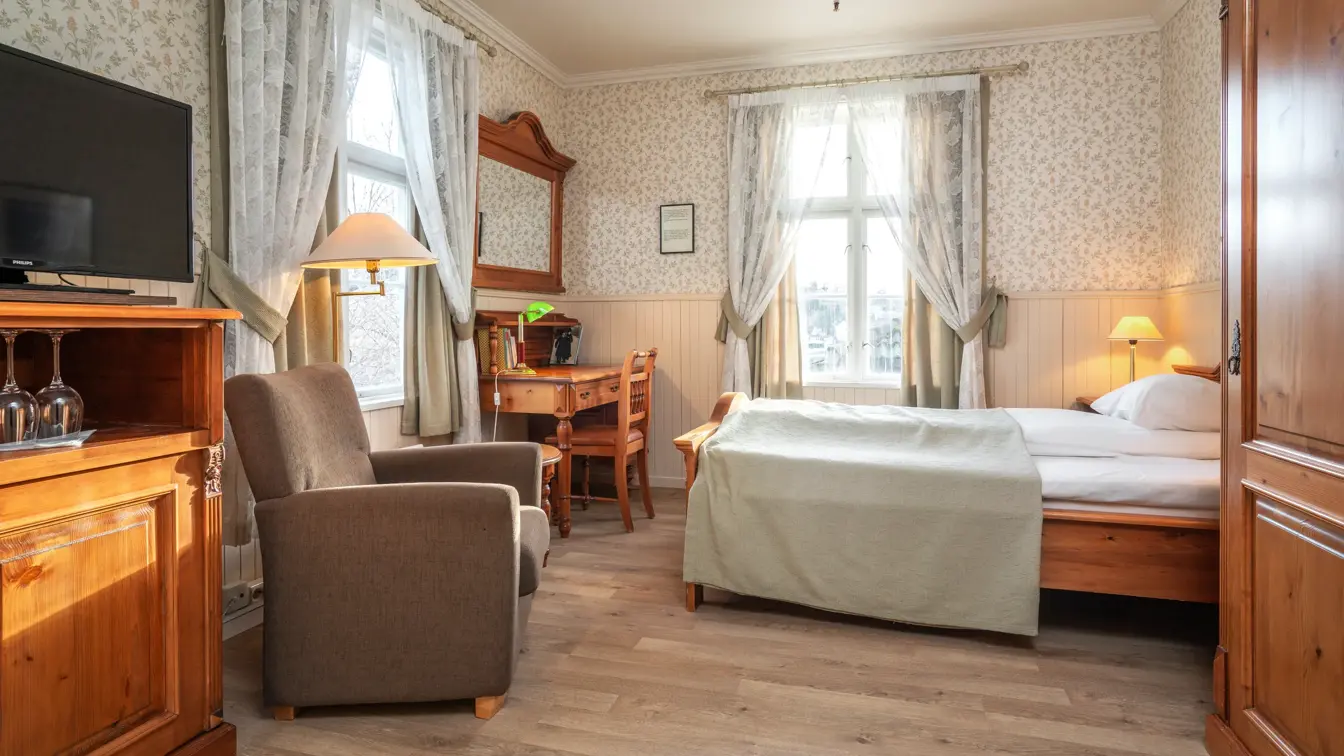 Dobbeltseng, skrivebord, skap med TV og lenestol i superior room