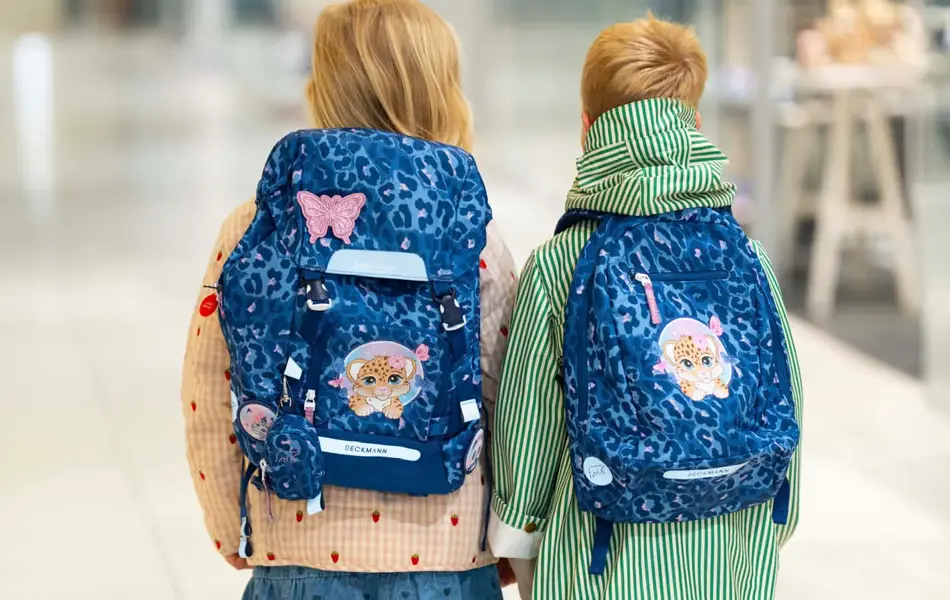 Jente og gutt med ryggen til kamera med blå skolesekker.