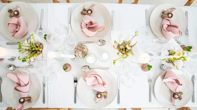 Langbord dekker til gjester med rosa servietter og grønn naturlig dekorasjon