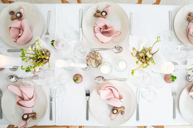 Langbord dekker til gjester med rosa servietter og grønn naturlig dekorasjon