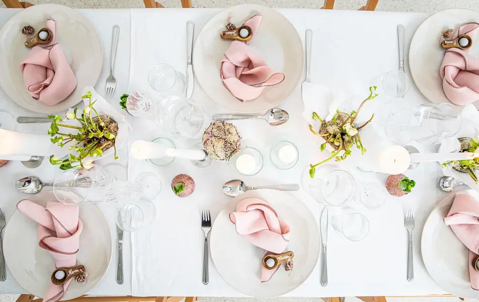 Langbord dekker til gjester med rosa servietter og grønn naturlig dekorasjon