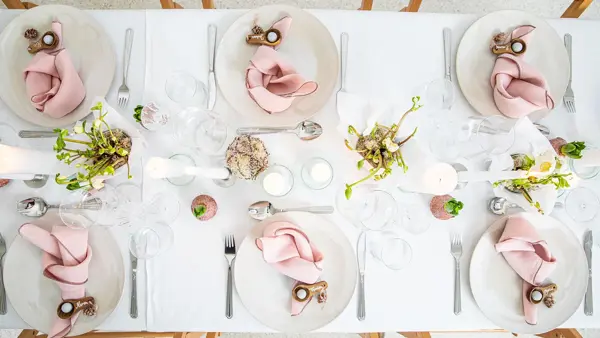 Langbord dekker til gjester med rosa servietter og grønn naturlig dekorasjon