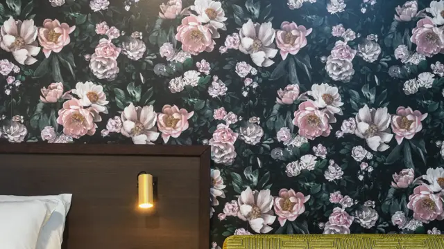 Detaljbilde av blomstrete tapet med store lyserosa roser, mørk sengegavl og en lime grønn sofa. I superior rom på Thon Hotel Høyers i Skien.