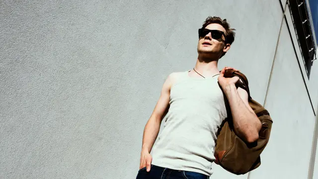 Mann med hvit singlett og skulderbag går ned trapp 